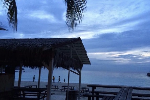 傍晚多云天空下热浪岛海滩上的草屋和木凳 