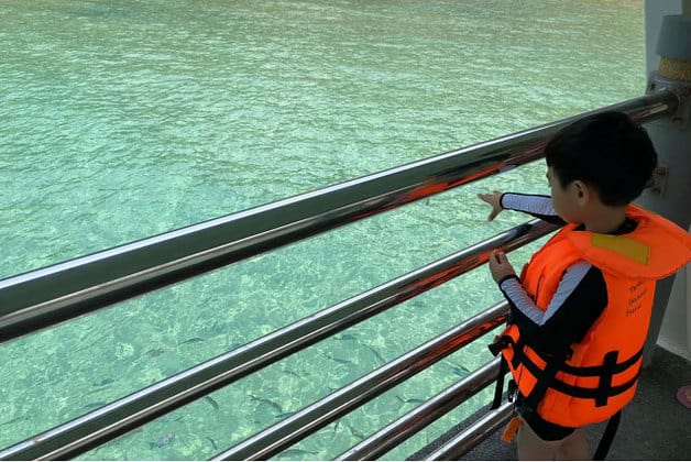 boy in orange life jacket standing on tioman island jetty bridge watching fish in the sea