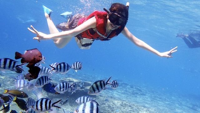 woman in red life jacket snorkeling under clear seawater with plenty tropical colorful fishes in pulau redang