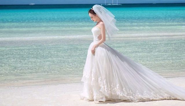 刁曼岛穿着白色长袍和面纱的新娘站在海滩上