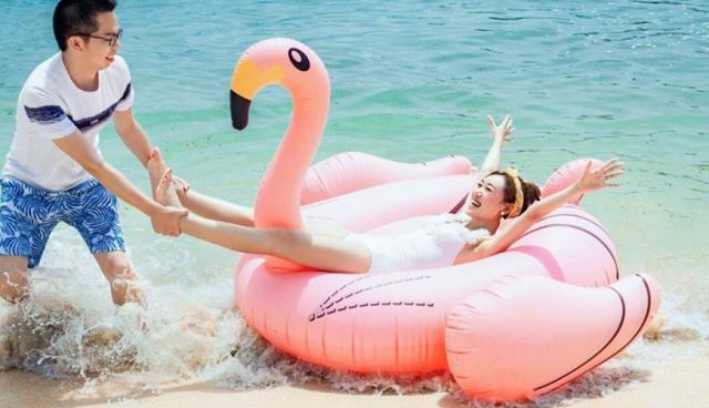 man pulling feet of his laughing girlfriend on a water floating inflatable flamingo on Tioman island beach