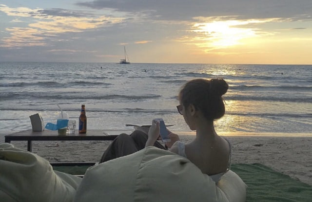 浪中岛女人正坐在海滩的豆袋上玩手机