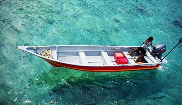 A man is sitting in a boat floating on clear sea water