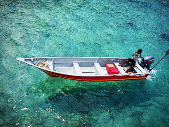 浪中岛一个人坐在一艘漂浮在清澈海水上的小船