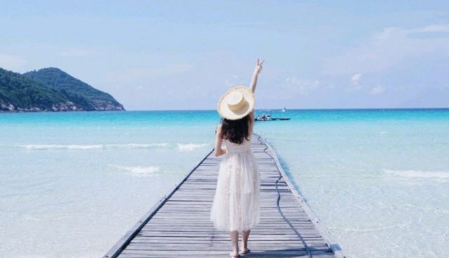 停泊岛身着白色连衣裙的女人站在清澈湛蓝的海水上方的码头