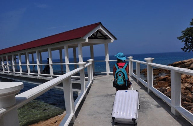 woman heaving white suitcase walking on the bridge of perhentian island jetty