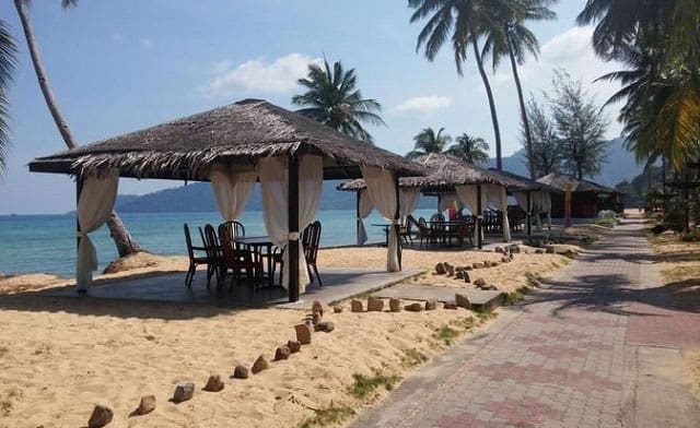 big straw umbrellas with dining table and chairs beneath on pulau tioman island beach