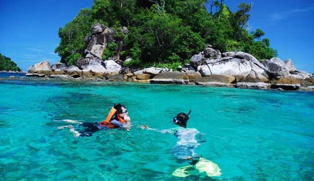 热浪岛两个人在清澈的绿色海水中浮潜背景有岩石和树木的美丽景色