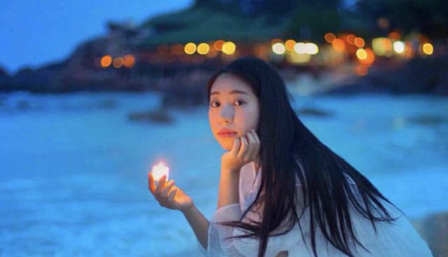 woman in white dress squat in pulau redang long beach with a candle light in her palm at twilight