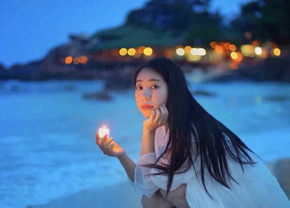 woman in white dress squat in pulau redang long beach with a candle light in her palm at twilight