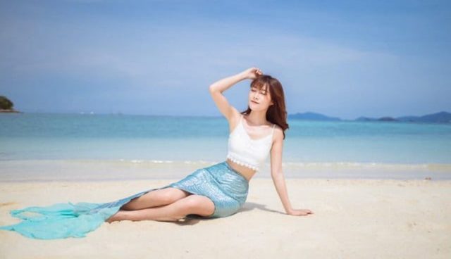 热浪岛充足的阳光和穿着美人鱼尾巴服装的女人坐在沙滩上