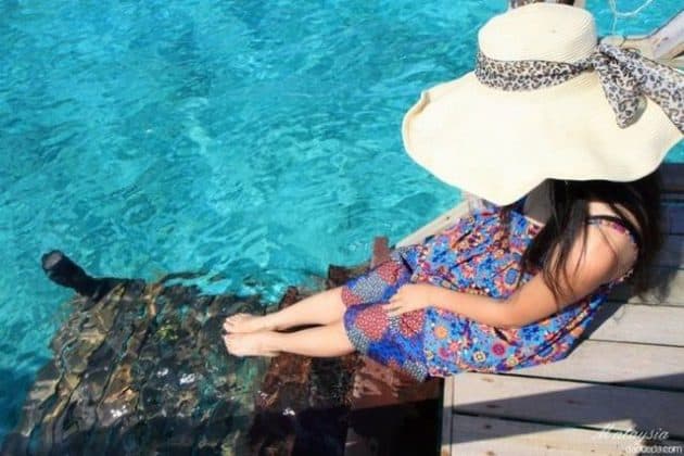 woman in white straw hat soaking feet in clear green tioman island sea