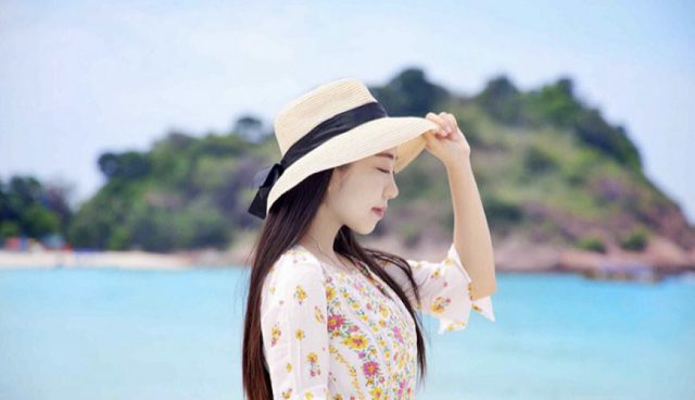 woman in floral dress and straw hat standing on redang beach with blue sea in the distance