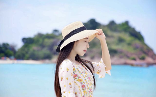 woman in floral dress and straw hat standing on redang beach with blue sea in the distance