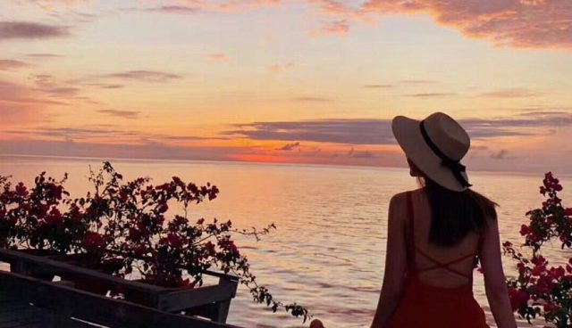 停泊岛戴草帽穿着红裙的女人在看日落和大海