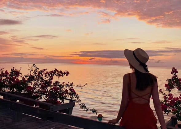 停泊岛戴草帽穿着红裙的女人在看日落和大海