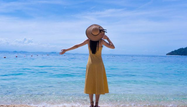刁曼岛站在海滩上的女人戴着草帽和黄色连衣裙