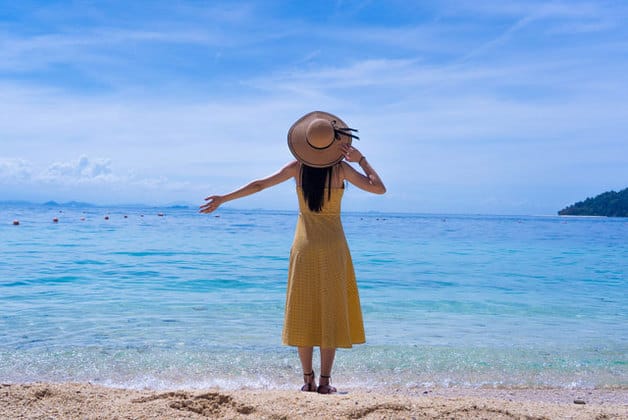 刁曼岛站在海滩上的女人戴着草帽和黄色连衣裙