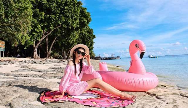 刁曼岛海滩上身着粉色西装的女人坐在漂浮的火烈鸟旁边