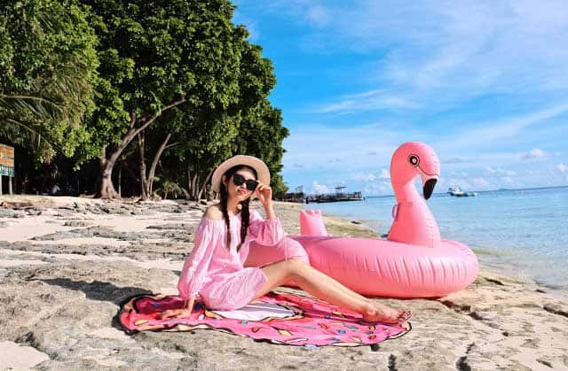 刁曼岛海滩上身着粉色西装的女人坐在漂浮的火烈鸟旁边