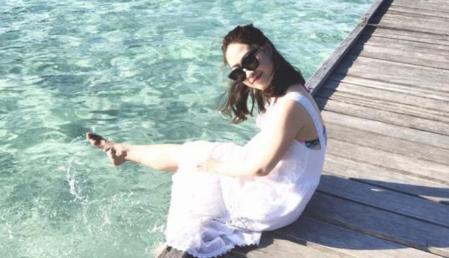 热浪岛穿着白色连衣裙的女人坐在清澈的海水上方的木桥上