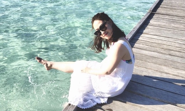 woman in white dress sitting on wooden bridge above clear redang sea water