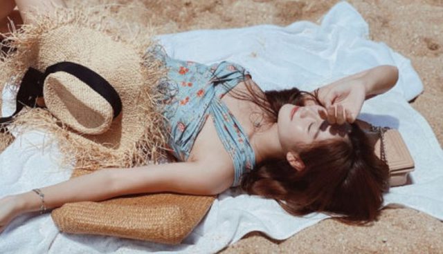 woman lying on beach towel with swimsuit and straw hat in redang island
