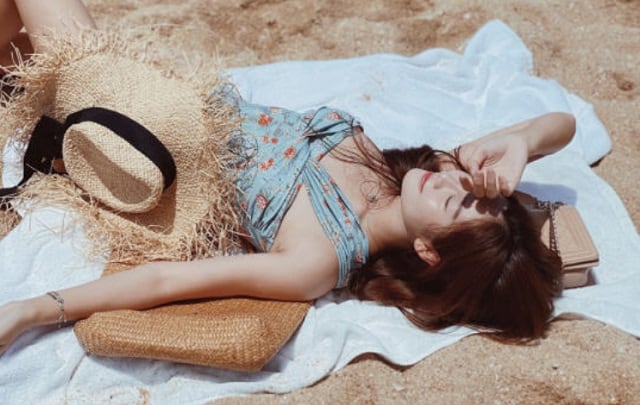 热浪岛女子穿着泳衣旁边放着草帽躺在沙滩巾上