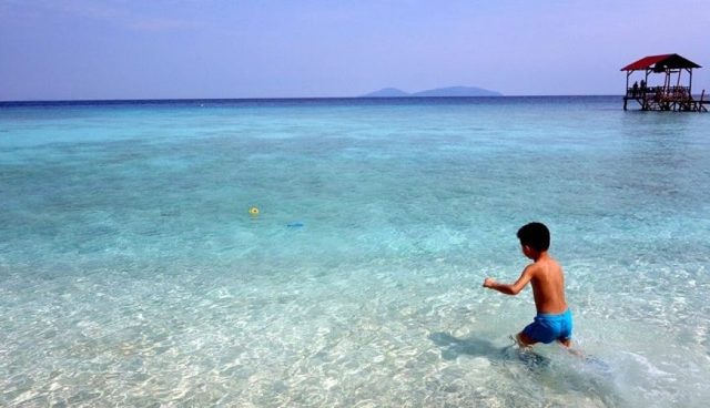 boy walking in clear sea water of pulau besar island
