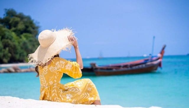 诗巫岛坐在海滩上的黄色花裙和大草帽的女孩