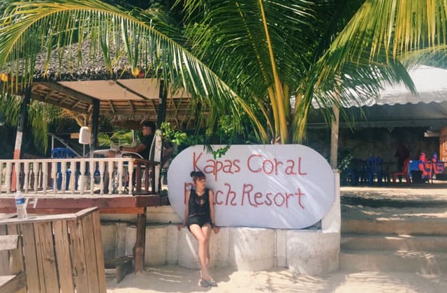 woman standing in front of kapas coral beach resort sign board on beach