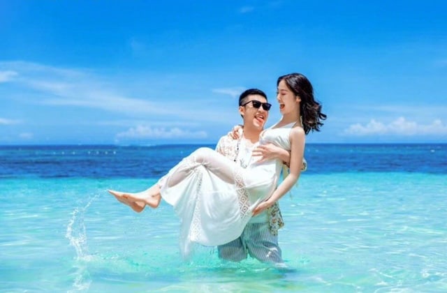 man holding woman in white dress laughing happily above the sea of kapas island