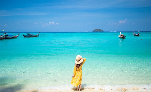 伯沙岛一位身着黄色裙子和戴着草帽的女人在海滩上的背影