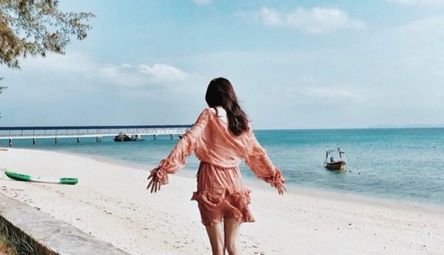 棉花岛一位身着粉红色连衣裙的女士站在海滩上而远处是码头