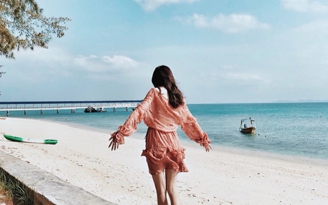 back view of a woman in pink dress standing on beach of pulau kapas with jetty in the distance