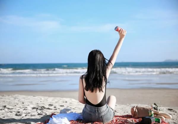 woman with black long hair sitting on beach of tinggi raising one hand