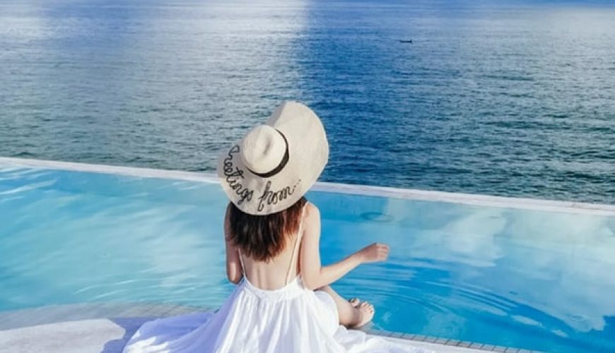 戴着大白草帽身穿白色连衣裙的女人坐在丁宜岛度假村的游泳池前