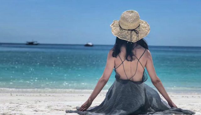 woman back view sitting at pulau tinggi beach with straw hat