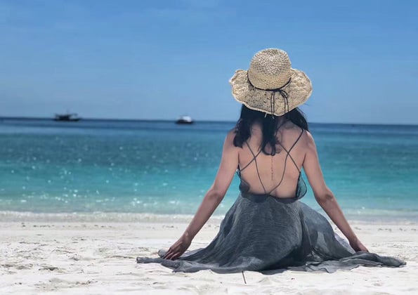 woman back view sitting at pulau tinggi beach with straw hat