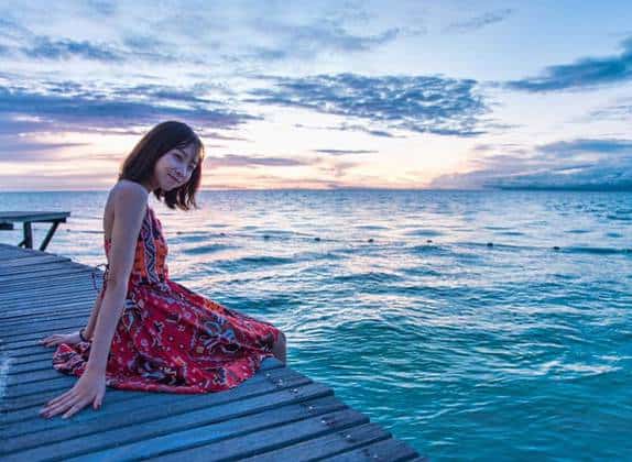 woman in floral red dress stting on wooden bridge above sea water of pemanggil island