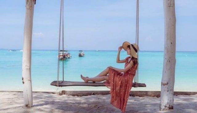 woman in red floral dress and straw hat sitting on a swing on pemanggil island beach