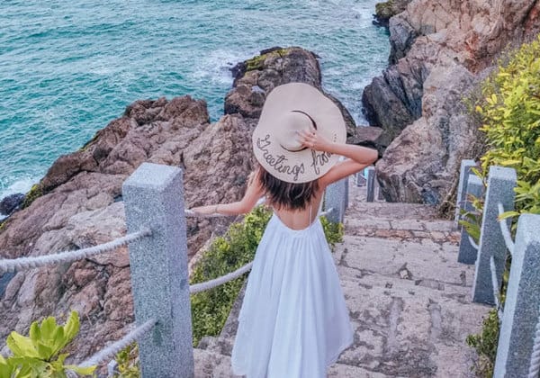 woman with big straw hat walking towards aur island sea on reef stairs