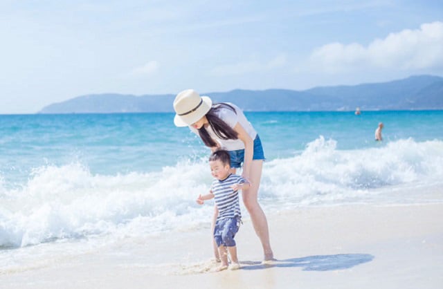 年轻的妈妈和蹒跚学步的男孩正在天鹅岛的海滩上散步