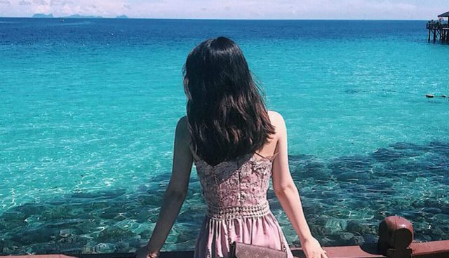 woman in pink dress looking at clear blue sea of aur island