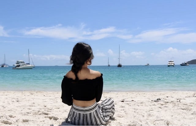 丽贝岛黑色抹胸长辫子的女人坐在面对蓝色大海的海滩上