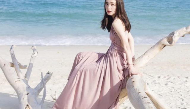 woman in pink tee dress sitting on koh lipe island beach in front of clear sea water