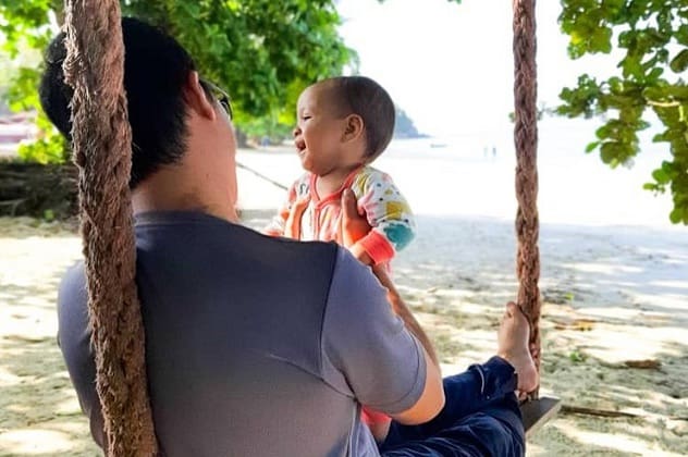 棉花岛爸爸抱着宝宝坐在海滩的秋千上