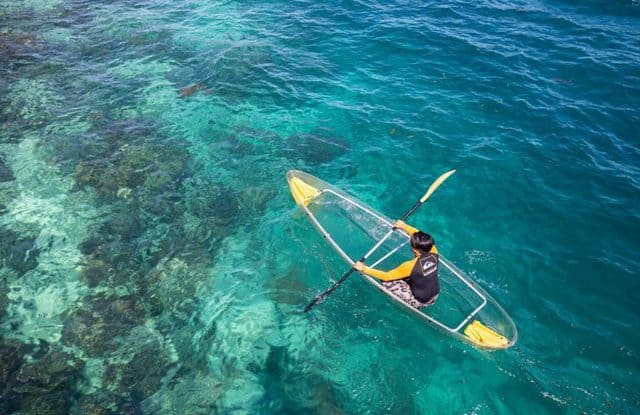 man rowing glass boat on clear seawater of mabul island