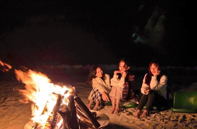 three women sitting on tenggol island beach next to campfire at night
