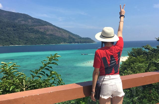 woman in red shirt and white short standing on hill top enjoy the view of koh lipe island sea